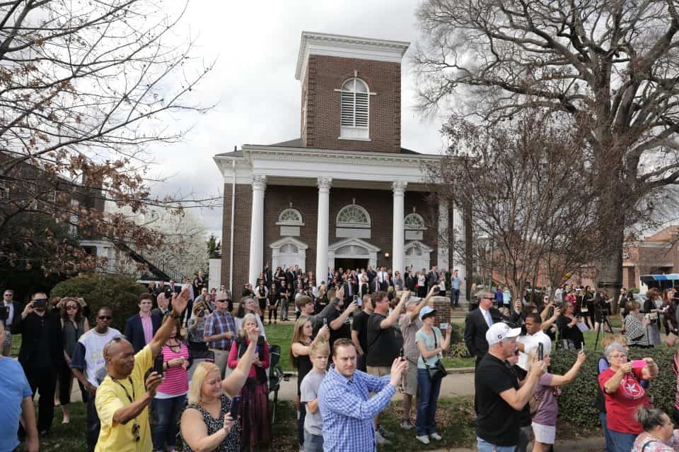 People gathered to catch a glimpse or a photo as Billy Graham's motorcade stopped at his childhood church in Charlotte. Grace Covenant Church was formerly Chalmers Memorial Associate Reformed Presbyterian Church, which was five miles from the Graham family's home. Church bells rang out as the motorcade paused there for one minute.