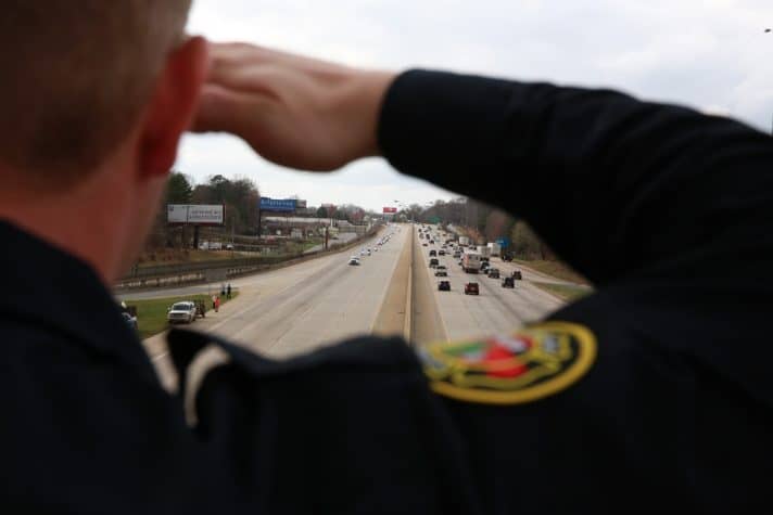 An officer salutes the motorcade as it approaches. The motorcade was made up of 14 cars led by eight North Carolina Highway Patrol officers.