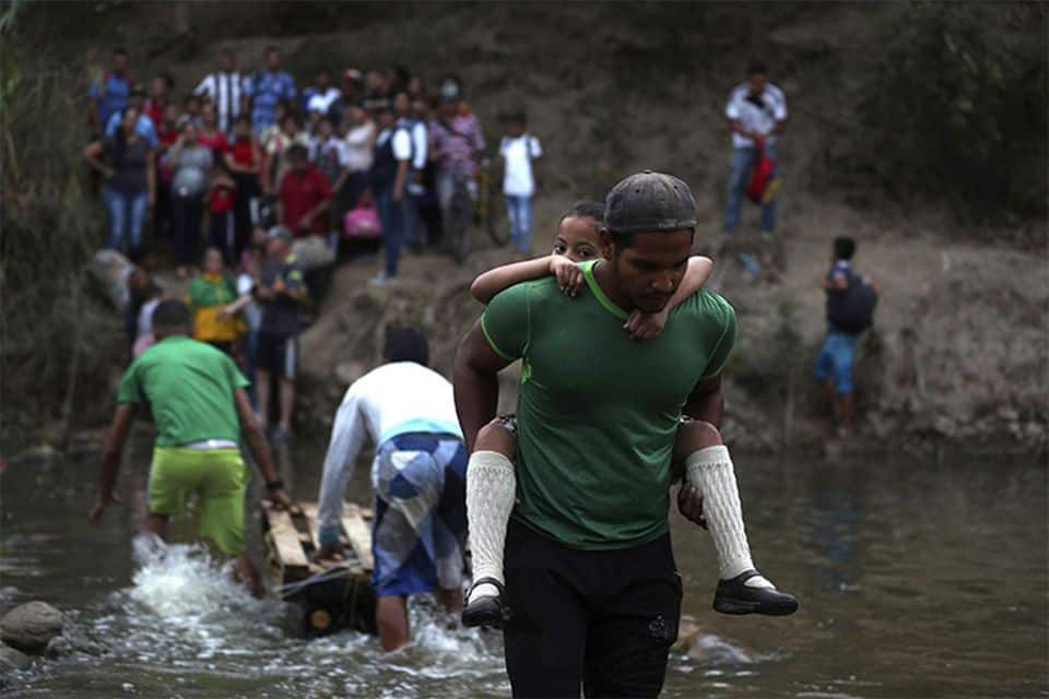 On Easter weekend, April 19-20, Franklin Graham will share the Gospel at the Festival de Esperanza (Festival of Hope) in the border town of Cúcuta, Colombia. Here, a man gives a Venezuelan student a piggyback ride across the Tachira River from Venezuela into Colombia. (AP Photo/Martin Mejia)