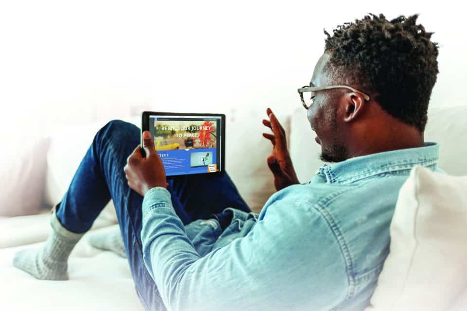 Shot of a handsome young man using his digital tablet while sitting on a sofa at home. Positive black man in casual reclining on sofa, using digital tablet, home interior.